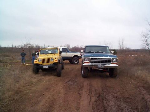 1978 Ford Bronco - Three modified trucks are parked on a muddy dirt road under an overcast sky.