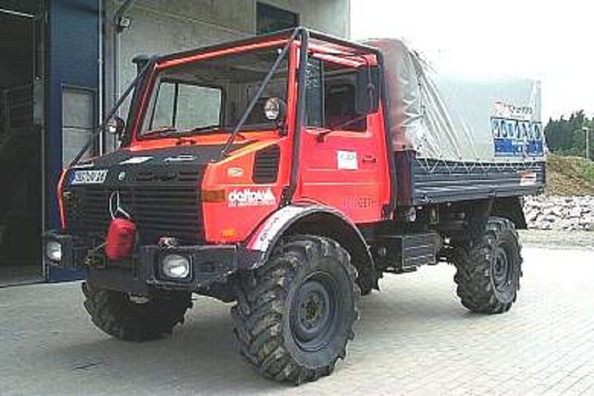Red Unimog truck with a tarped bed parked outside a building