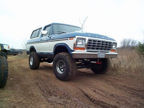 1978 Ford Bronco - A lifted 1978 Ford Bronco with two-tone paint sits on a muddy track, with another vehicle visible in the background.
