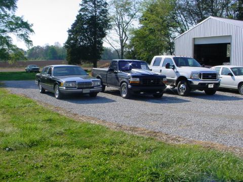 1972 Ford Ranchero - Several vehicles are parked on a gravel lot next to a white building.