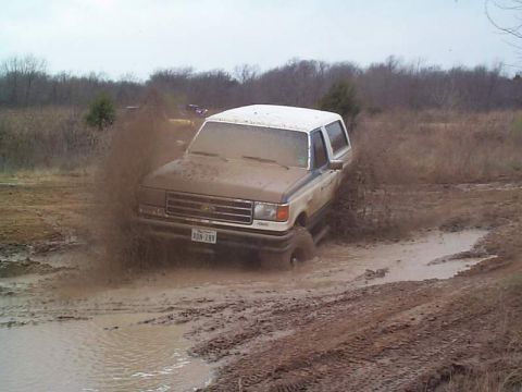 1978 Ford Bronco - A Ford Bronco navigates a muddy terrain, sending dirt flying.