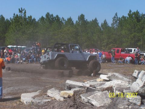 1989 Ford Bronco - A Jeep navigates an obstacle course during an outdoor event, with spectators gathered around.