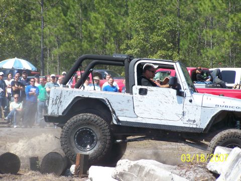 1989 Ford Bronco - A white Jeep Wrangler Rubicon navigates an obstacle course with spectators gathered.