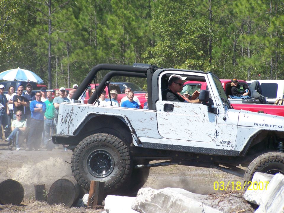 White Jeep Wrangler Rubicon driving over logs with people watching