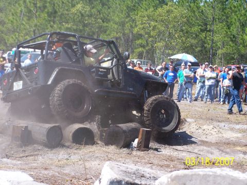 1989 Ford Bronco - Jeep Wrangler tackles an off-road course with onlookers present.