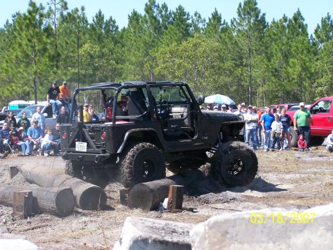 1989 Ford Bronco - A modified black Jeep Wrangler navigates an obstacle course with spectators watching.