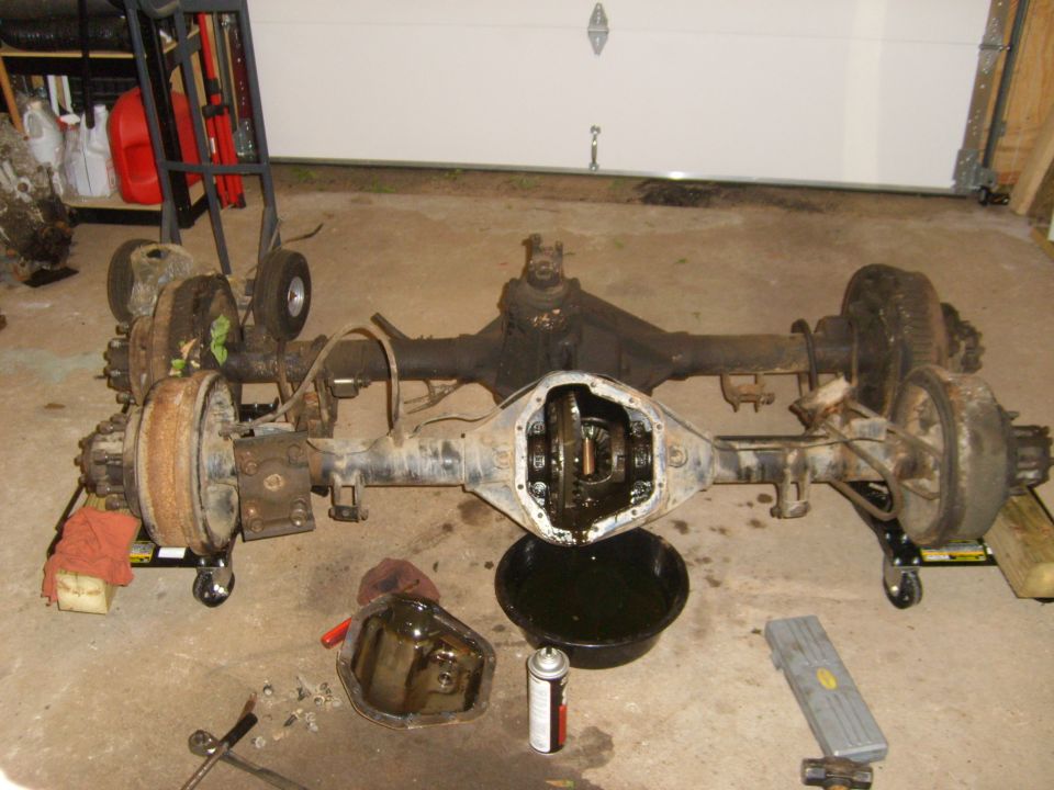 1994 Ford Bronco rear axle assembly with differential exposed, sitting on dollies. Oil pan and spray can nearby