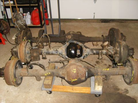 1994 Ford Bronco - Close-up view of two vehicle axles, one with a black differential cover, resting on wooden stands.