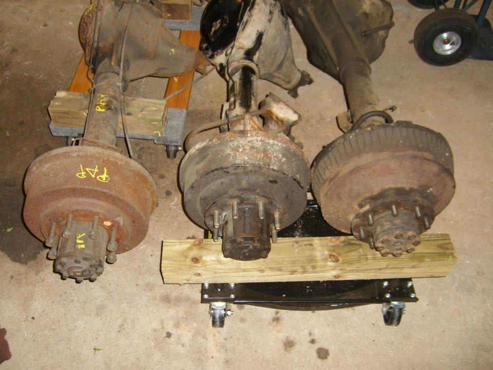 Three solid axle housings with brake drums and hubs on a garage floor