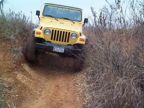 1978 Ford Bronco - A yellow Jeep Wrangler navigates a muddy off-road trail.