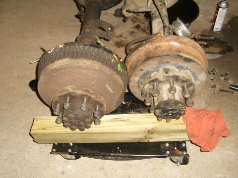 1994 Ford Bronco - Two rusty axles with brake drums and hubs are displayed on a dolly, suggesting they are parts for a vehicle.