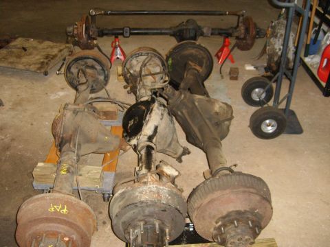 1994 Ford Bronco - Multiple vehicle axles are shown in a garage setting, some with brake drums attached.