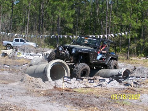 1989 Ford Bronco - A black Jeep Wrangler navigates an obstacle course with concrete pipes in the mud.