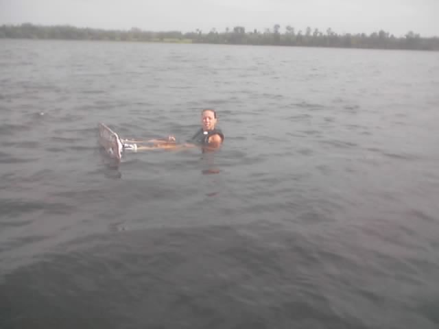 Person in a life vest floating in a lake holding a board, no vehicle visible