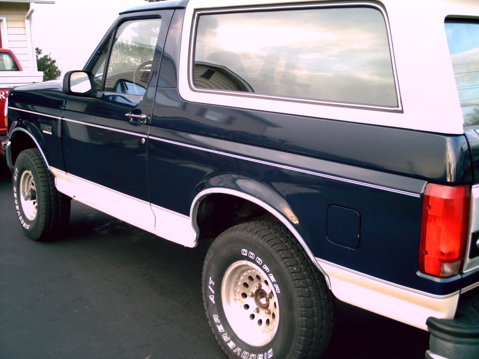 Dark blue and white Ford Bronco parked on asphalt. Side view shows front fender, door, and rear quarter panel