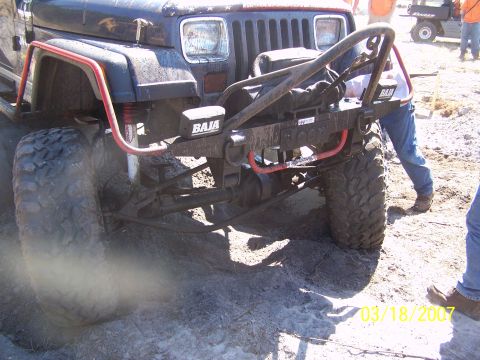 1989 Ford Bronco - A heavily modified Jeep Wrangler is shown in a muddy, off-road setting with people and another vehicle nearby.