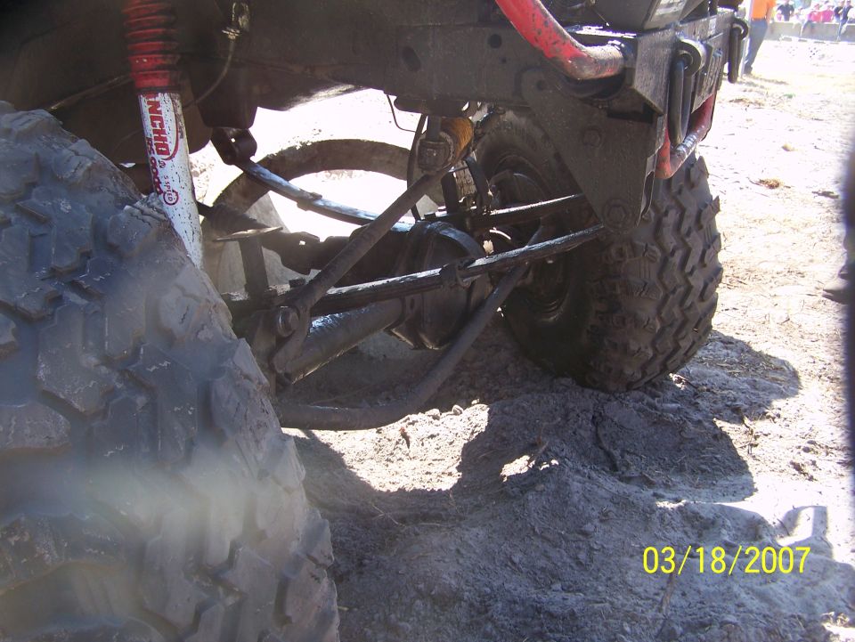 Muddy off-road vehicle rear suspension with large tire and red shock absorber