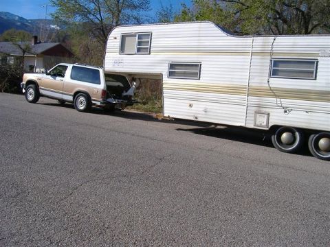 1968 Ford Mustang - A two-tone SUV is hitched to a large travel trailer, parked on a residential street.