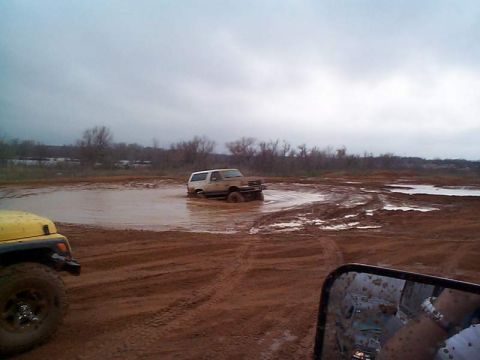 1978 Ford Bronco - Two off-road vehicles navigate a muddy terrain with one vehicle partially submerged in a large puddle.