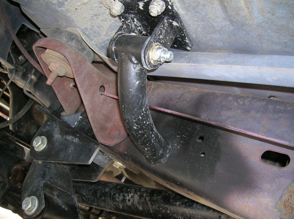 Underbody close-up of a black bent bar bolted to a welded frame bracket on a truck