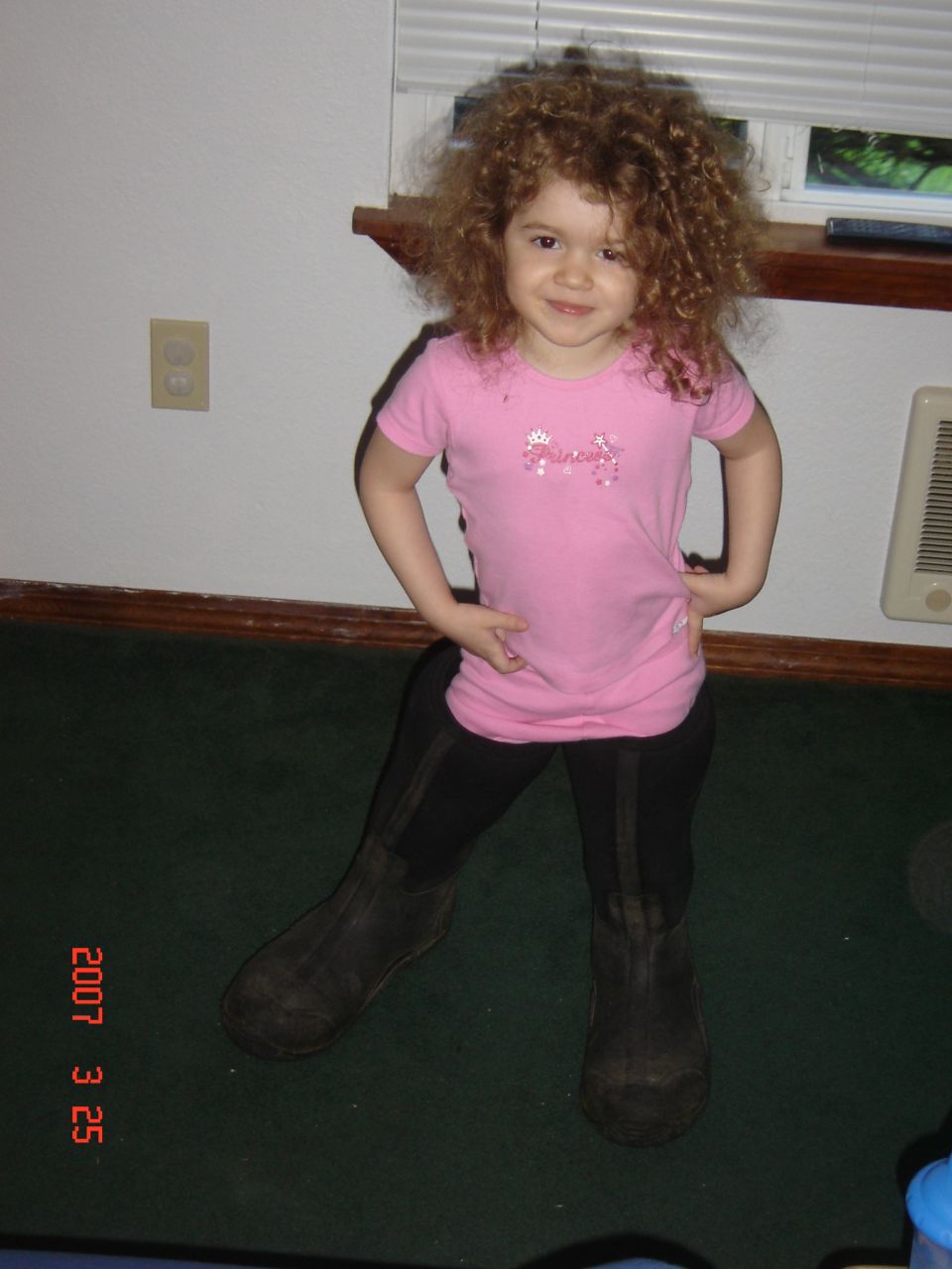 Child with curly hair wearing a pink shirt and black boots