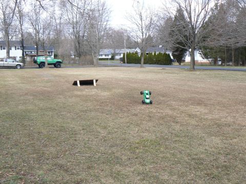 1994 Ford Bronco - A remote control car sits on a grassy field near a lifted SUV and a wooden ramp.