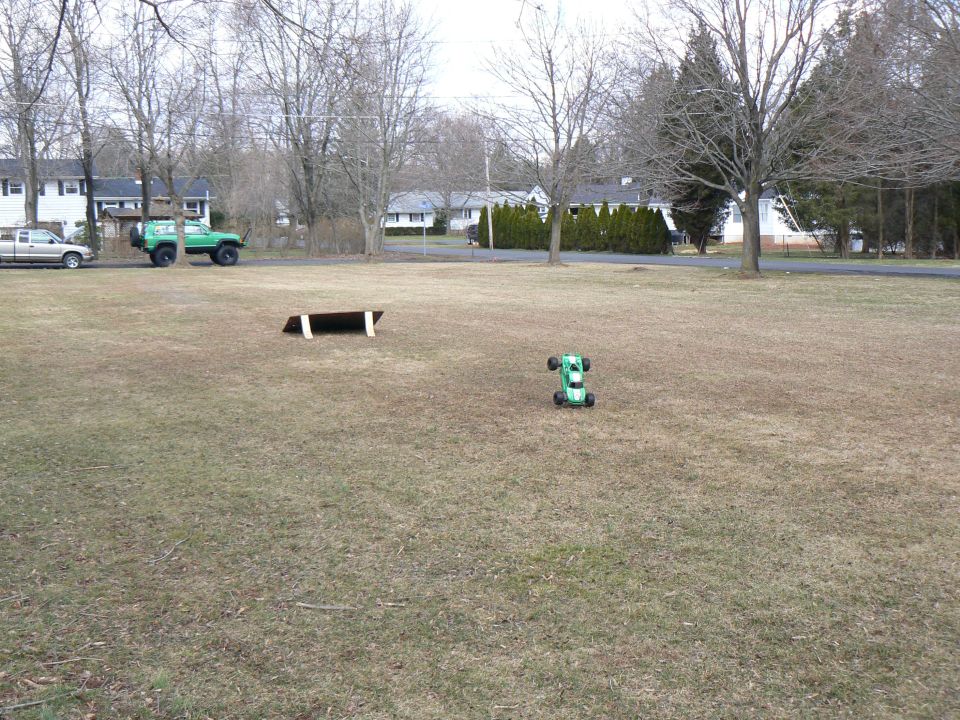 Green remote control car on grass with a lifted green SUV parked nearby