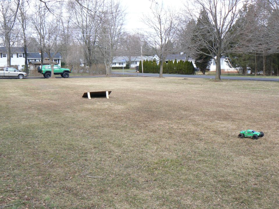 green off-road vehicle and a green RC car on a grassy field with houses in background