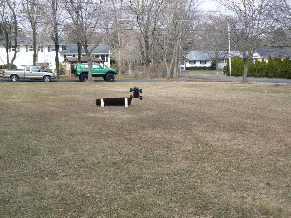 Green SUV with large tires parked on grass, a silver pickup truck is parked nearby