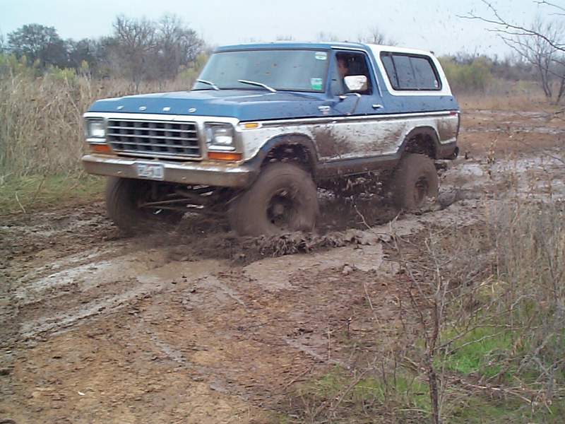 Blue and white Ford Bronco stuck in mud, front-left wheel deep in muck