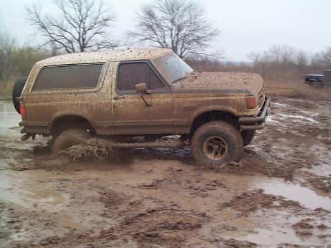 1978 Ford Bronco - A muddy Ford Bronco navigates a challenging off-road terrain, with another vehicle visible in the background.