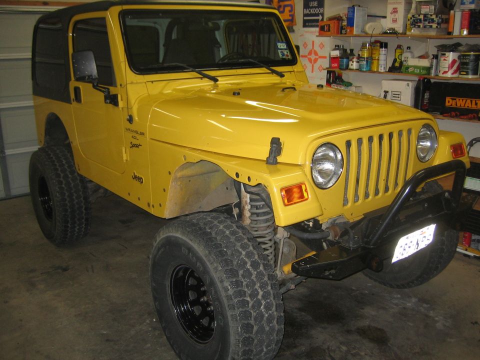 Yellow Jeep Wrangler TJ with fender flares removed showing bare fenders in a garage