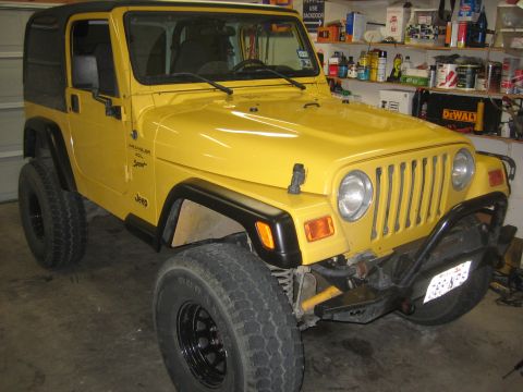 2001 Jeep Wrangler - A yellow 2001 Jeep Wrangler is parked in a garage, showing its front-right side and black soft top.