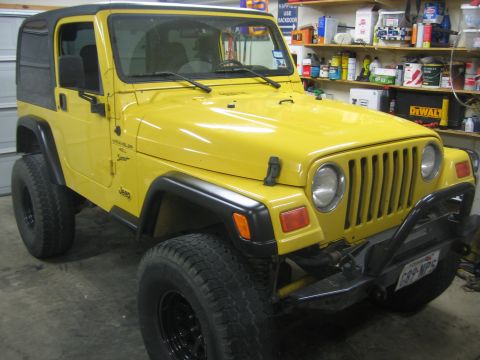 2001 Jeep Wrangler - Yellow Jeep Wrangler TJ with a black soft top parked in a home garage, shot from the front three-quarter passenger side. Body-side badging…