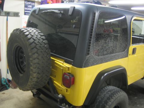 2001 Jeep Wrangler - Rear view of a yellow 2001 Jeep Wrangler, showing the spare tire and hardtop.