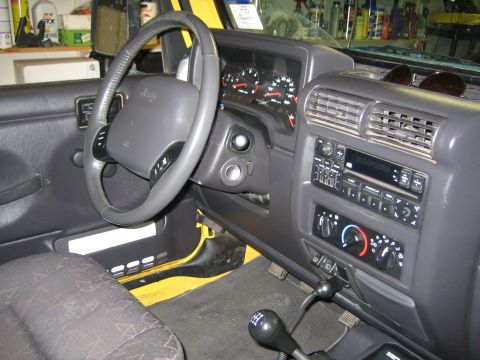 2001 Jeep Wrangler - The interior of a Jeep Wrangler, the dashboard, steering wheel, and center console with radio and climate controls.