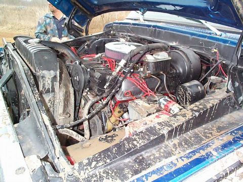 1978 Ford Bronco - The engine compartment of a blue truck is shown, heavily coated in mud and dirt.