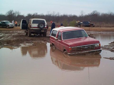 1978 Ford Bronco - A red Ford Bronco is stuck in a muddy puddle, with another white SUV nearby also in the mud.