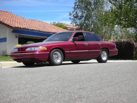 1992 Ford Crown Victoria - A maroon sedan is parked on the street in front of a house.