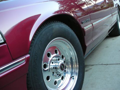 1992 Ford Crown Victoria - The side profile of a maroon 1992 Ford Crown Victoria is shown, focusing on the front wheel and fender area.