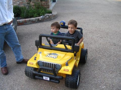 1986 Ford Bronco - Two children sit in a yellow toy Jeep, with a man standing nearby.