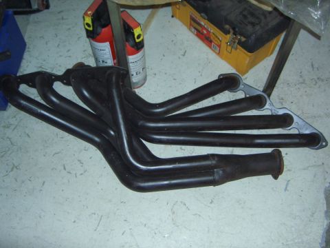 1974 Ford Bronco - A black exhaust manifold with six pipes and a flange is shown on a concrete floor.