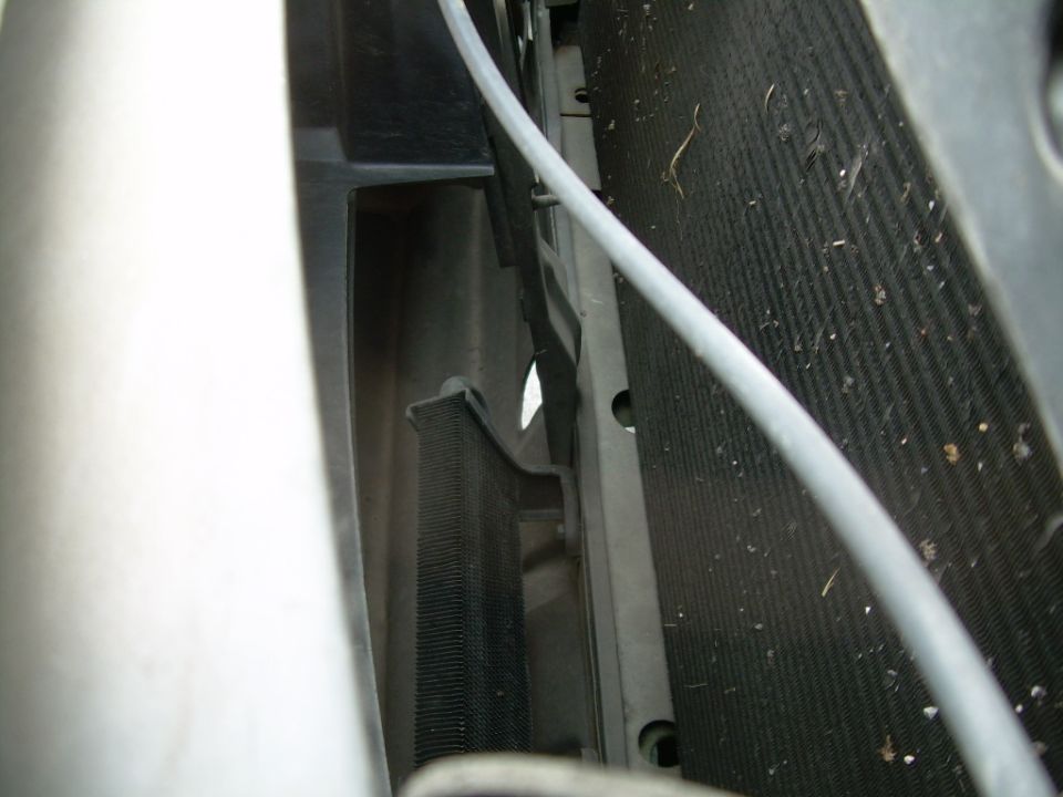 Close-up of vehicle's radiator and condenser fins, with a gray hose running across