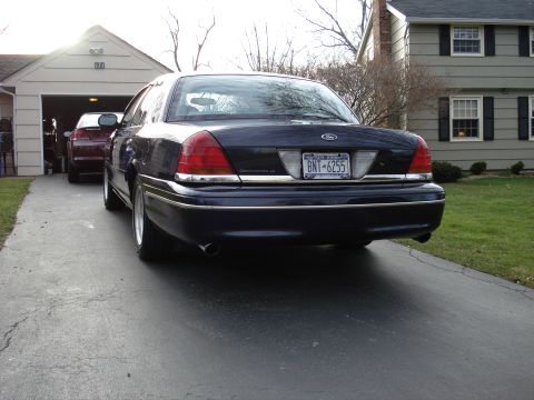 2000 Ford Crown Victoria - A dark blue 2000 Ford Crown Victoria is parked in a driveway, with another car visible in the garage behind it.