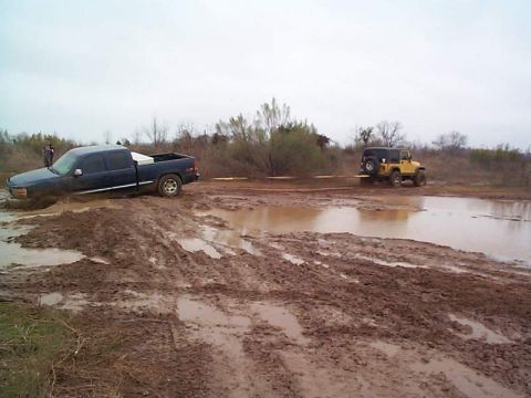1978 Ford Bronco - Two off-road vehicles are stuck in a muddy terrain after attempting to navigate through a waterlogged area.