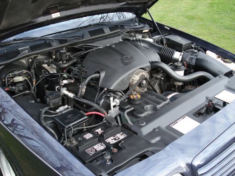 2000 Ford Crown Victoria - Engine bay of a dark blue Ford sedan photographed from the driver's side with the hood open, showing the modular V8 under its black Ford-ov…
