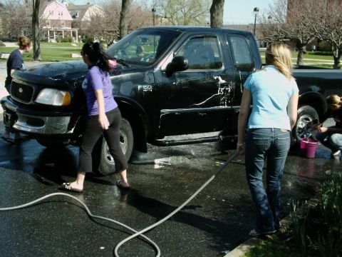 1997 Ford F-150 - People are washing a black Ford F-150 pickup truck with soap and water on a paved surface.