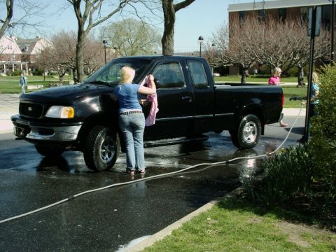 1997 Ford F-150 - A woman washes a black 1997 Ford F-150 pickup truck on a wet asphalt surface.