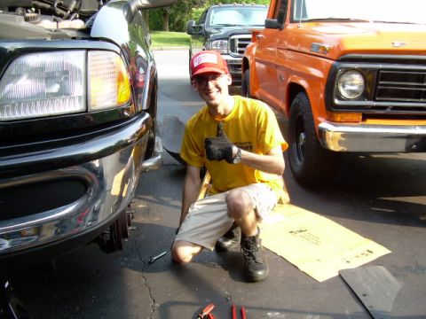1997 Ford F-150 - A man is working on a black truck, with an orange truck parked nearby. The orange truck's grille suggests it's from the 1970s.