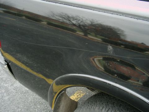 1997 Ford F-150 - Scratched black side panel of a 1997 Ford F-150 with a yellow line and tire visible.